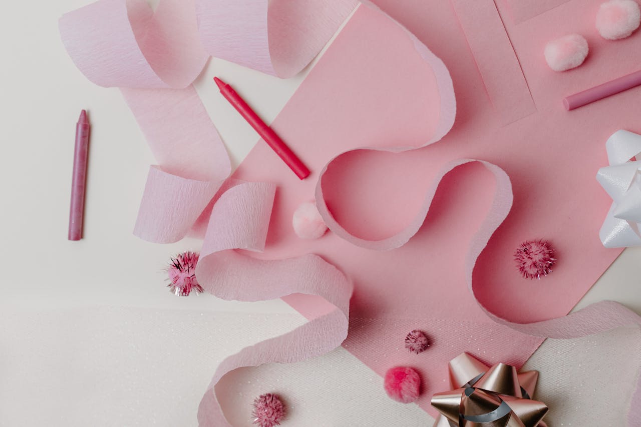 Flat lay of pink craft supplies and decorations featuring ribbons and bows on a pastel background.